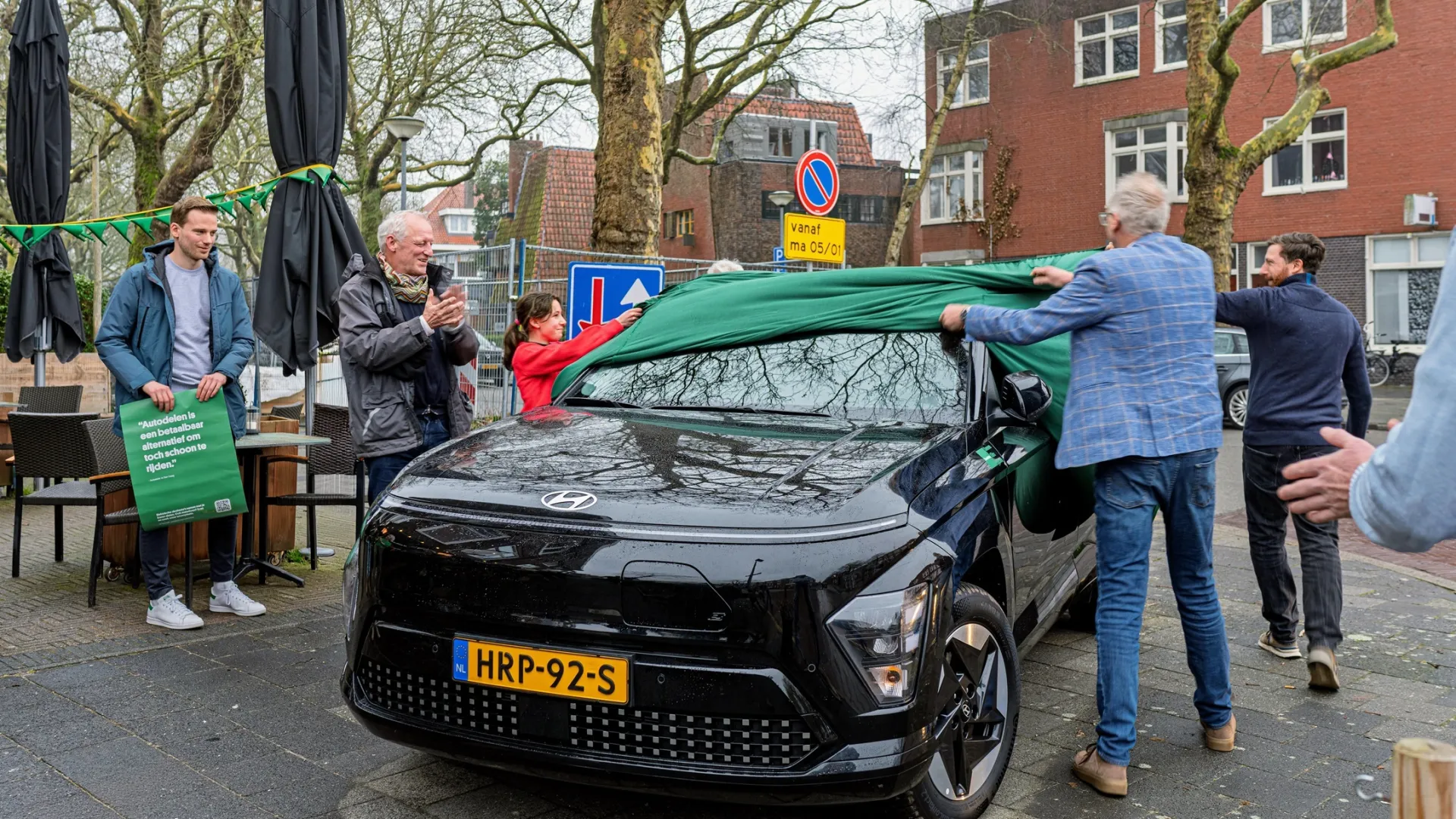Mensen onthullen een nieuwe zwarte auto op een plein.