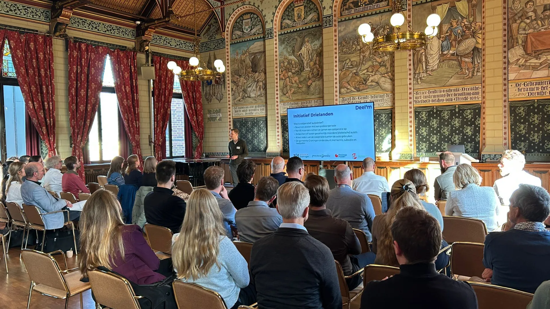 Groep mensen woont een presentatie bij tijdens communitybijeenkomst in Drenthe op 30 oktober 2025.
