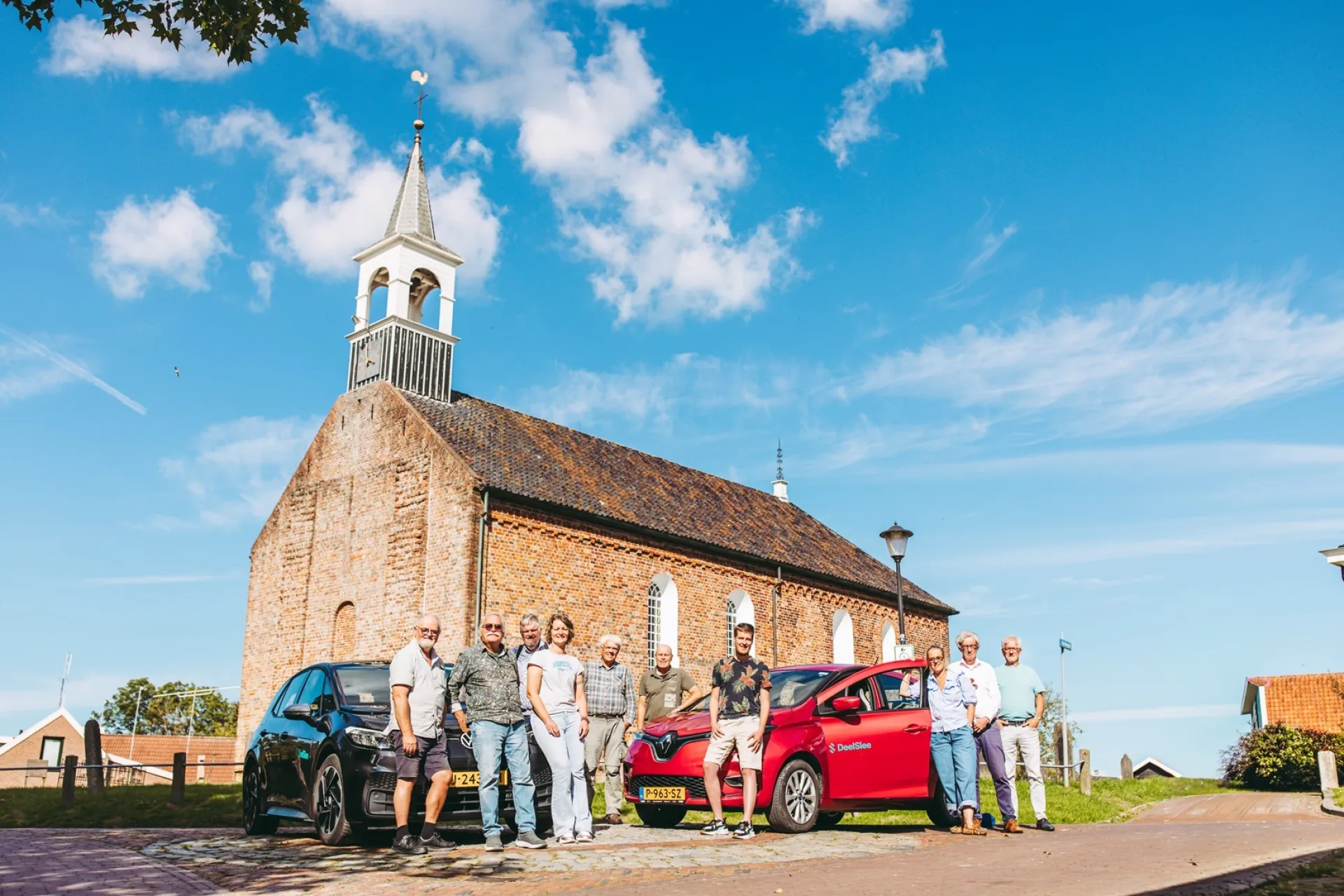 Mensen poseren met deelauto's van Deelslee voor een historische kerk. 