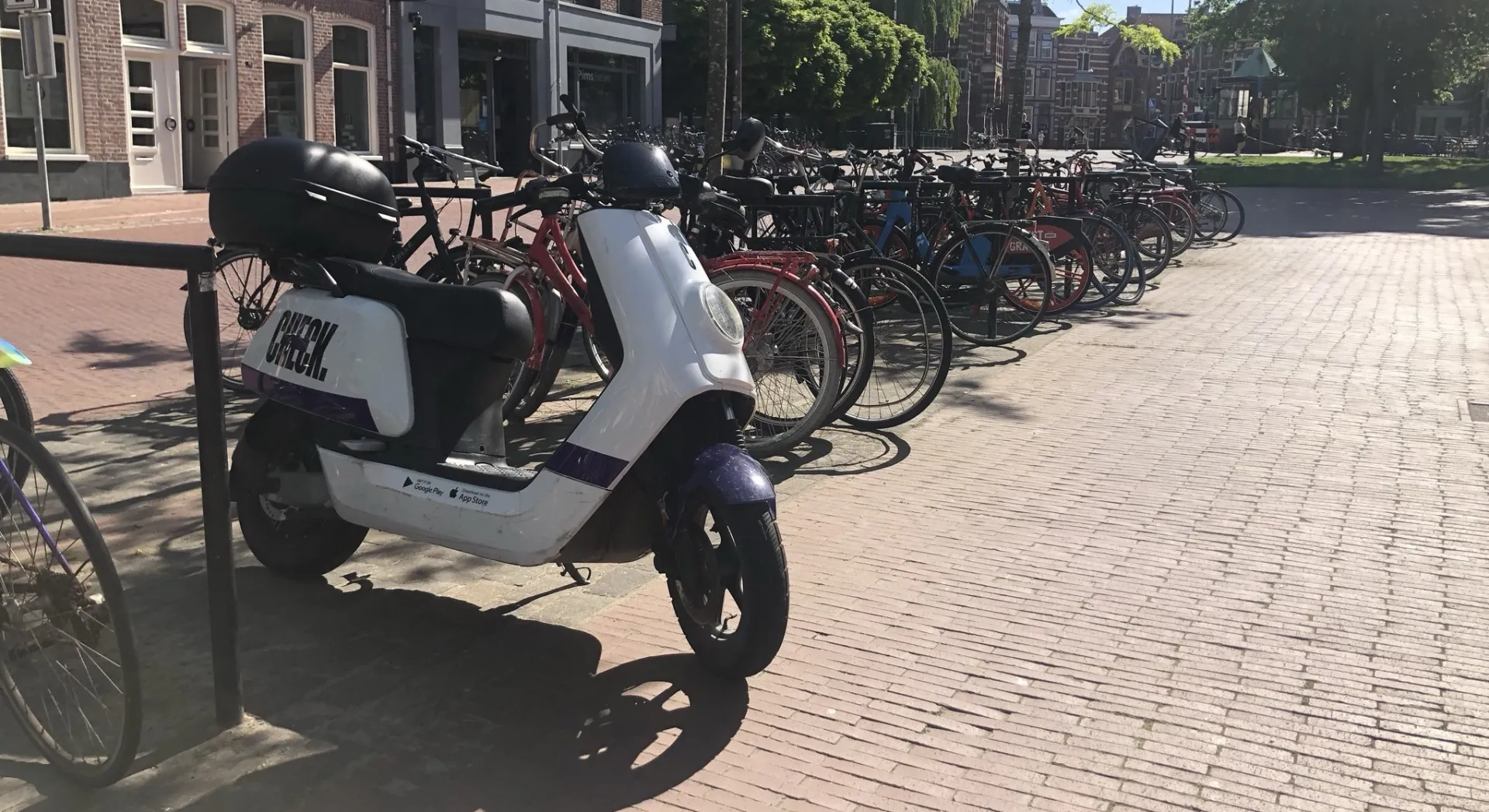 Scooter en fietsen geparkeerd op een zonnige straat.