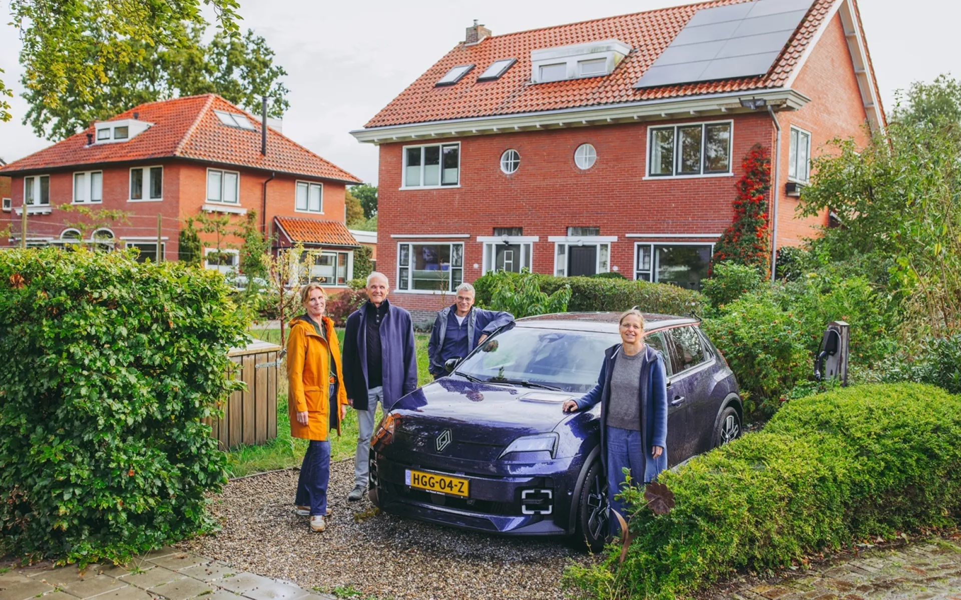 Een groepje mensen poseert voor een huis met zonnepanelen en een blauwe deelauto.