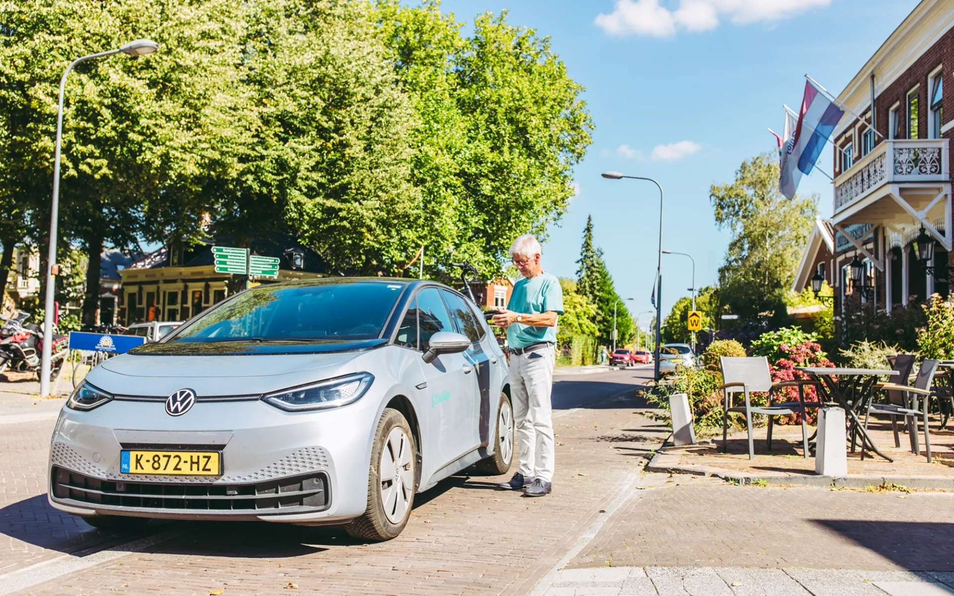 Elektrische auto geparkeerd op een zonnige straat met een persoon ernaast.