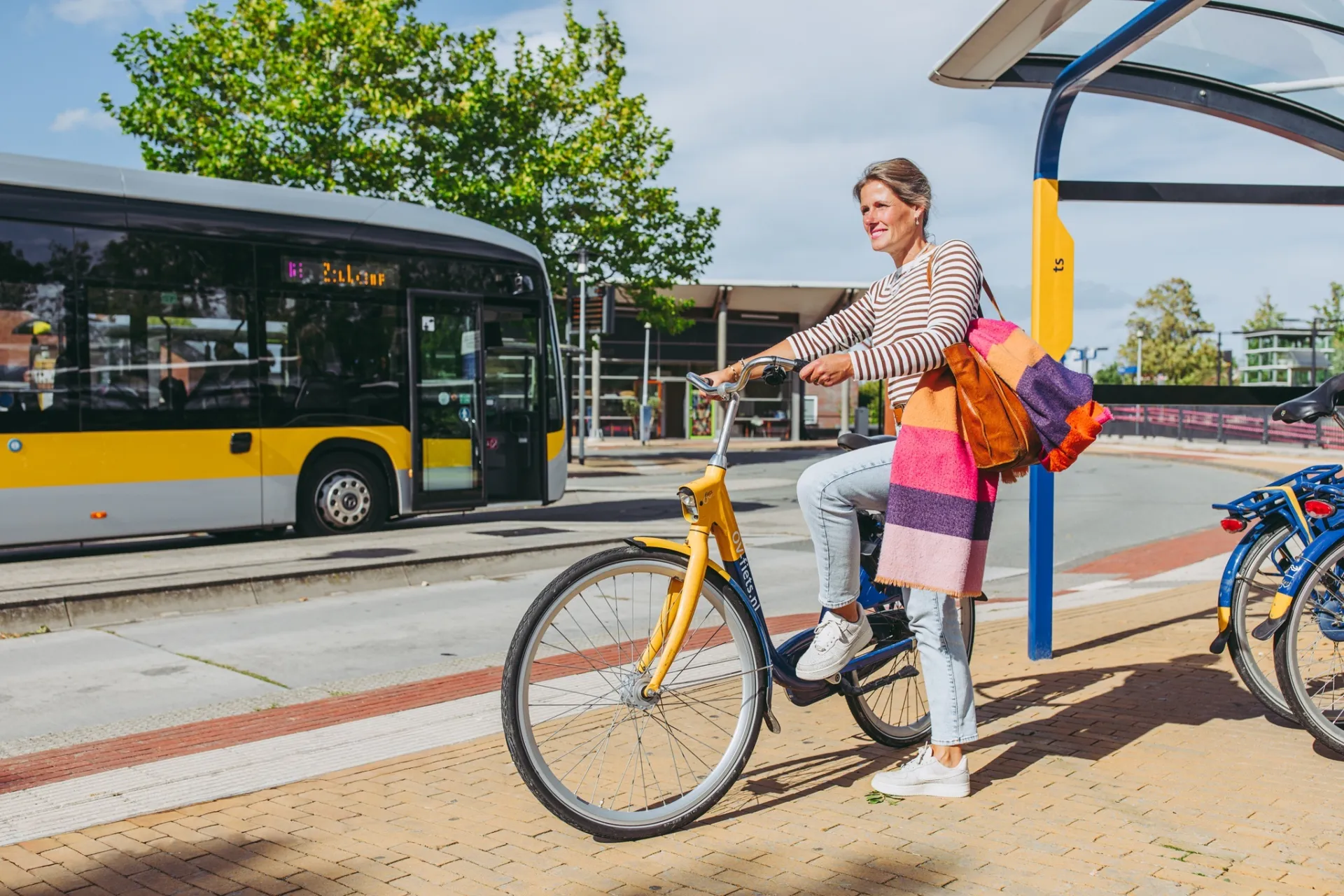 Vrouw op fiets bij bushalte op zonnige dag.