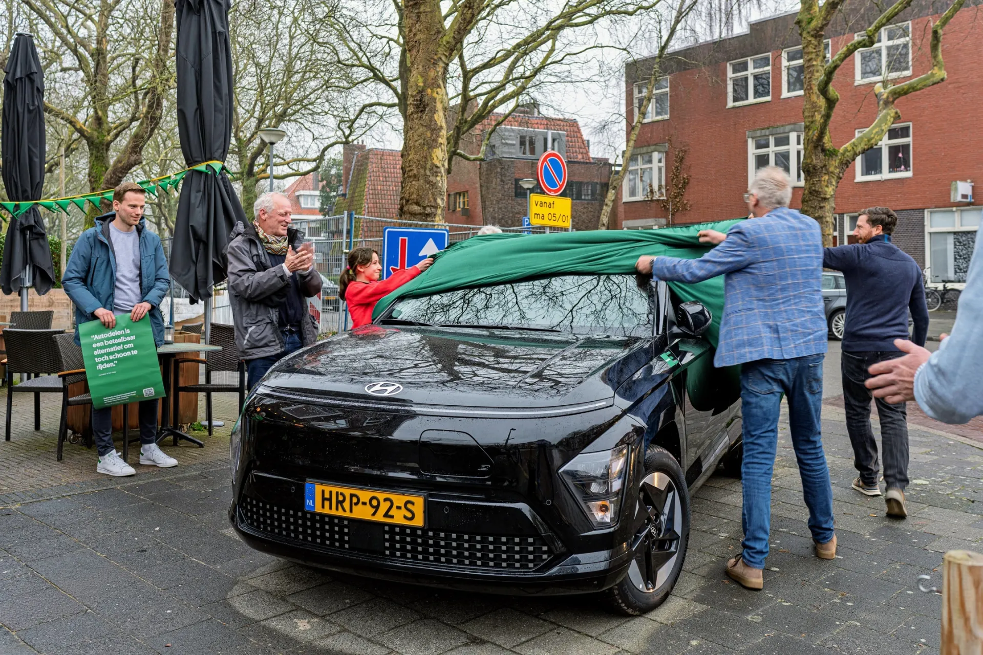 Mensen onthullen een nieuwe zwarte auto op een plein.