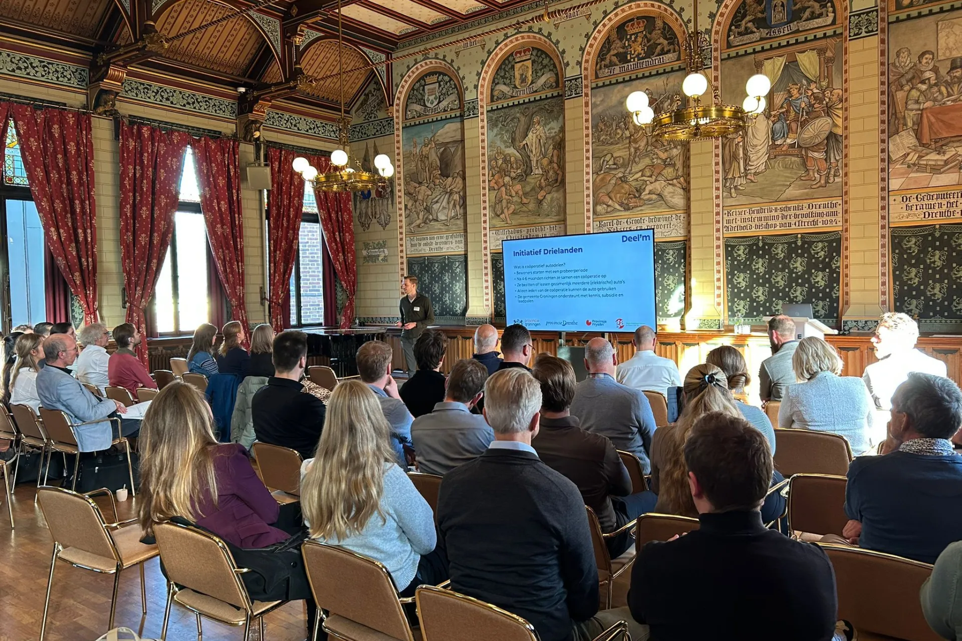 Groep mensen woont een presentatie bij tijdens communitybijeenkomst in Drenthe op 30 oktober 2025.